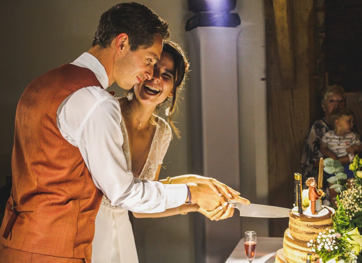 Un couple souriant coupe un gâteau de mariage au milieu d'une célébration.
